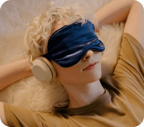 Person relaxing with headphones and a sleep mask, symbolizing rest, relaxation, and mindfulness.
